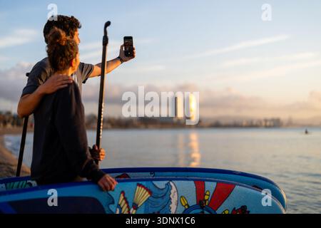 Two friends capture a social media style travel moment by taking a sunset selfie on the beach Stock Photo