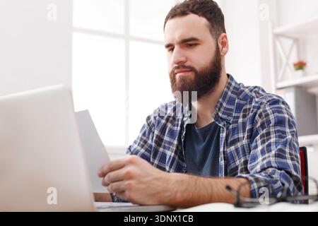 Close up of a serious man office worker is reading report, while is sitting at the table with open net-book. Stock Photo