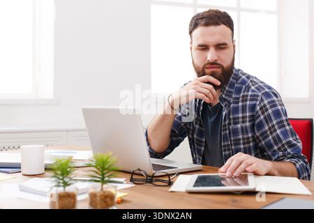 Close up portrait of a serious young businessman sitting and using tablet computer in office Stock Photo