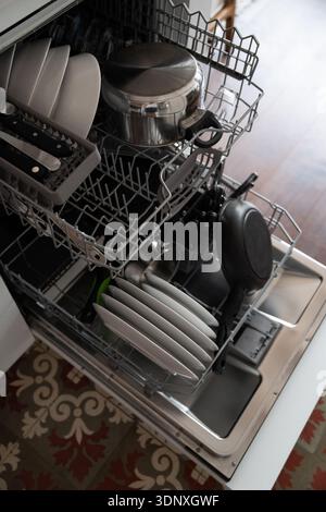Open dishwasher with clean dishes, pots, pans, and cutlery inside, showing a modern kitchen appliance simplifying household chores and daily routine Stock Photo