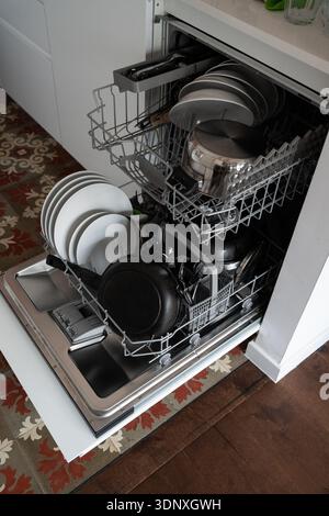 Dishwasher door open showing dishes, plates, bowls, pots, pans, and cutlery arranged inside, ready for a wash cycle in a contemporary kitchen Stock Photo