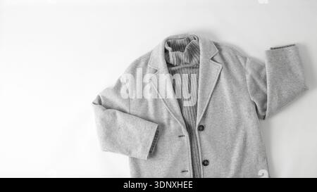 Monochrome look style. Light grey wool coat or jacket and cashmere sweater isolated on neutral fabric background. Autumn apparel. Trendy fashion. Stock Photo