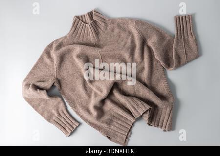 Soft sweater of taupe luxury natural cashmere wool lying on light grey background. Autumn and winter pure wool clothing. Knit apparel fashion. Stock Photo