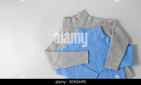 Soft warm sweaters of  grey and of  blue luxury natural cashmere lying on light neutral background. Autumn and winter pure wool clothing. Knit apparel Stock Photo