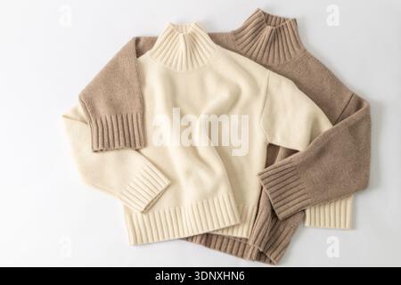 Soft warm pair sweaters of cream beige and taupe brown luxury natural cashmere lying on white fabric background. Autumn and winter pure wool clothing. Stock Photo