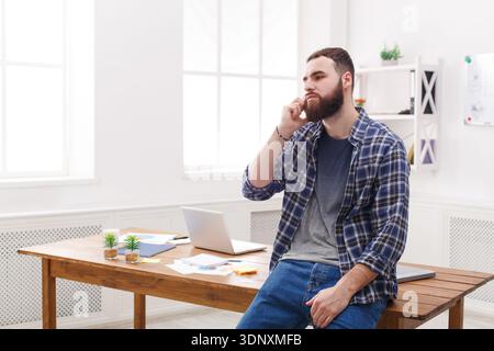 Pensive young businessman talking on mobile phone sits on the table Stock Photo