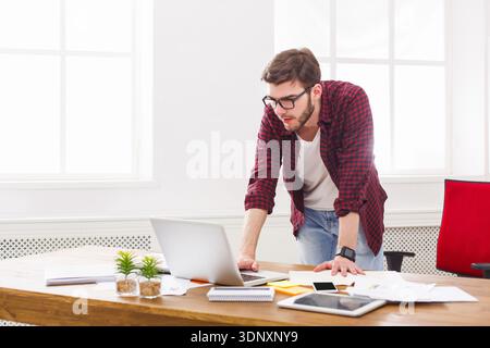 Young businessman standing by the laptop in modern white office Stock Photo