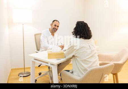 A professional psychologist conducts a session with a patient in a calming clinic environment. The bright and welcoming setting enhances the therapeut Stock Photo