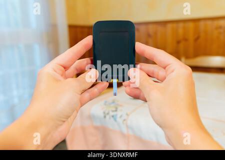 Close-up of hands holding a glucometer, a device for measuring blood sugar levels. Essential for diabetes management, it provides quick results for he Stock Photo