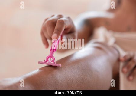 Close-up shot of a woman shaving her leg with a pink plastic razor. The focus is on the hand holding the razor, as it glides over smooth skin, showcas Stock Photo