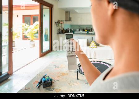 Cropped unrecognizable woman holding an air conditioner remote control while standing in a living room, pointing at a modern device to adjust settings Stock Photo