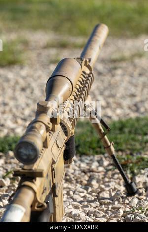 A detailed close-up of an airsoft sniper rifle with desert camouflage design, set against a rocky terrain, ideal for military training and airsoft ent Stock Photo