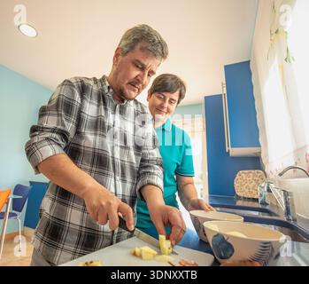 A couple enjoys a relaxed morning at home, preparing breakfast together in their kitchen. They chat and playfully interact, creating a warm, welcoming Stock Photo