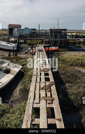 Image of an abandoned dock stretching into a dry sea basin, surrounded by grounded boats and weathered wooden structures, capturing a striking scene o Stock Photo