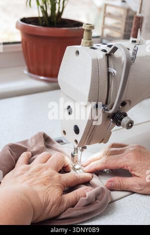 An elderly woman skillfully sews fabric using a sewing machine, highlighting her passion for tailoring. A perfect representation of productive aging a Stock Photo