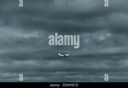 An airplane flies amidst a dramatic sky filled with dark, heavy clouds, creating a striking contrast with the bright aircraft. The scene captures both Stock Photo
