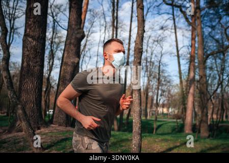 A young man trains actively in a lush green park, wearing a protective face mask for safety. He is focused and determined, embodying a healthy lifesty Stock Photo