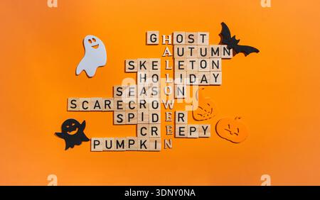 A vibrant Halloween themed crossword puzzle using wooden blocks on an orange background. Words like ghost and pumpkin are accompanied by playful cutou Stock Photo