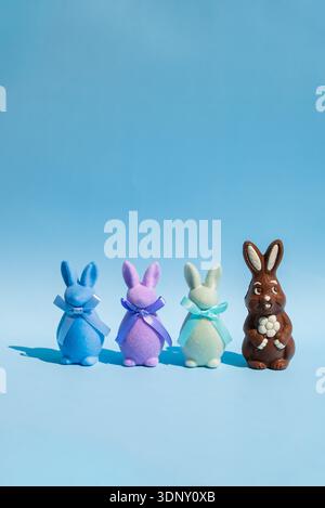 A still life featuring a chocolate Easter bunny with a flower, alongside three colorful felt bunnies with ribbons, set against a vibrant blue backgrou Stock Photo