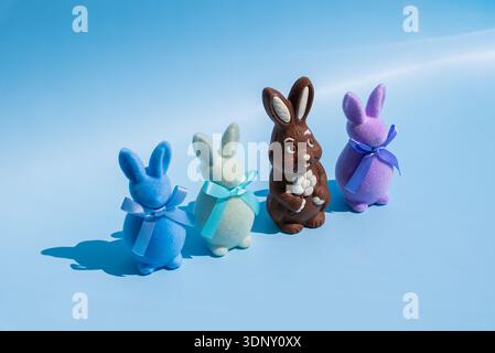 A whimsical Easter scene with a chocolate bunny surrounded by plush, ribboned bunnies in blue, green, and purple on a soft blue background, evoking fe Stock Photo