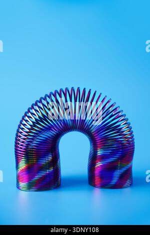 A colorful metal spring with neon hues forms an arch against a vivid blue background.. The abstract design highlights the fascinating play of light an Stock Photo