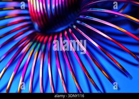 An abstract image of a vibrant neon spiral composed of twisted metal strips with a gradient of colors against a bright blue background, showcasing mod Stock Photo