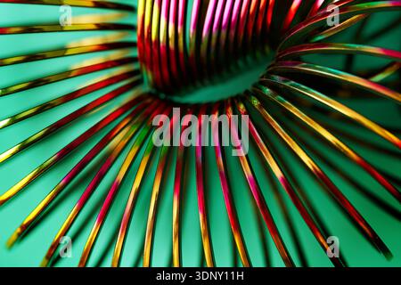 Close-up of a colorful metal spiral with vibrant neon hues against a smooth green background. The twisted coils create a dynamic, abstract, and eye-ca Stock Photo