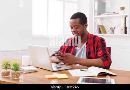 Happy black businessman in office at workplace with mobile Stock Photo