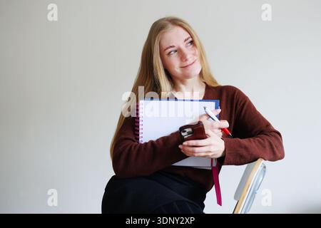 Female freelancer organizing tasks with notebook and phone. Work planning, time management and personal organization concept. Stock Photo