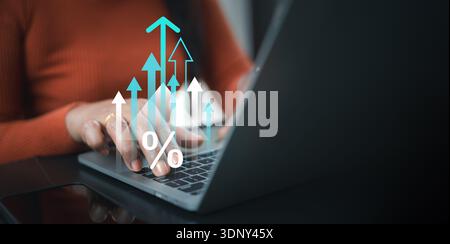 Business woman using laptop with virtual rising arrows and percentage icon, depicting interest rate increase, financial growth, investment profit, and Stock Photo