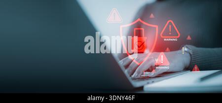 A woman professional uses a laptop with glowing red warning icons and digital shield overlay, representing data breach, hacker attack, and online secu Stock Photo