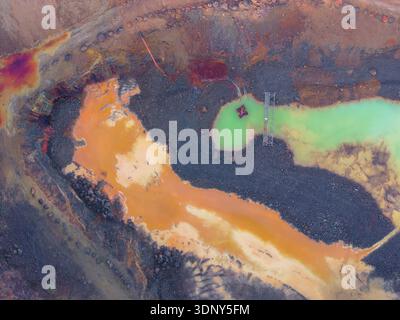 Aerial view of vividly colored pools of orange, green, and brown liquids contrasting with the dark earth, creating a surreal landscape, La Roche-Jaudy Stock Photo