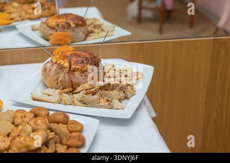 Assorted savory snacks buffet on white tablecloth with baskets of bread and baked dip in bread bowl, ready for guests at a casual party Stock Photo