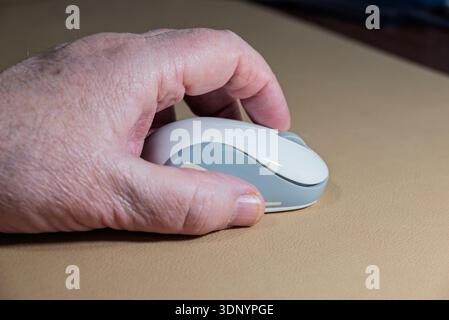 A person's hand is using a bluetooth computer mouse to navigate a digital interface attached to a computer Stock Photo