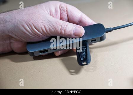 A hand inserts a USB drive into a multi-port adapter, likely for data transfer or device connectivity. Stock Photo