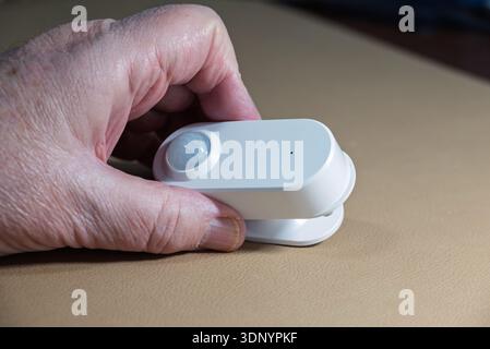 A hand holds a white motion sensor, likely for a smart home security system, to detect movement. Stock Photo