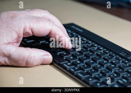 A person's hand is typing on a black portable USB charged bluetooth wireless keyboard, likely for work or communication. Stock Photo