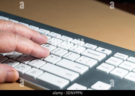 A person's hand is typing on a white keyboard, likely for work or communication. Stock Photo