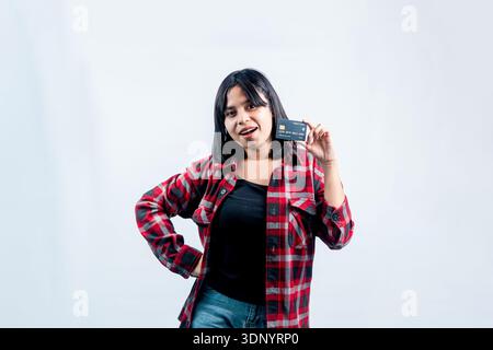 Young Southeast Asian woman in a red flannel shirt posing confidently while showing a black credit card, isolated on a clean white background. Stock Photo