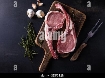 Fresh tomahawk raw steak. Dry aged raw tomahawk pork steak with herbs and salt on old wooden background. Preparing to grill. Stock Photo