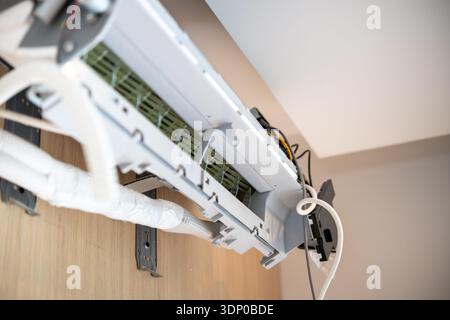 Interior view of a split-type air conditioner unit mounted on a wooden wall with visible wiring and insulated pipes during installation. Stock Photo