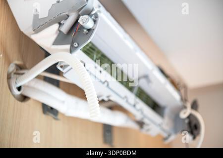 Close-up of a partially installed indoor split air conditioner unit mounted on a wooden wall in a residential environment. Stock Photo