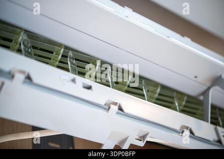 A closeup view of a white domestic air conditioner unit mounted on an interior wall with its front panel open, showing internal air vents and componen Stock Photo