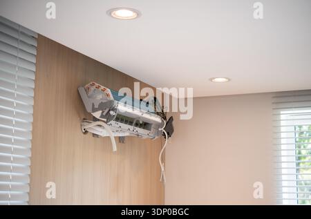 Unfinished wall-mounted domestic air conditioner unit installed on wooden panel wall inside a modern home with window blinds and recessed ceiling ligh Stock Photo