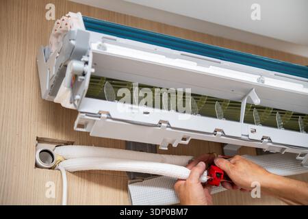 Technician hands install pipes and tubing on a wall-mounted domestic air conditioner unit inside a residential setting. Stock Photo