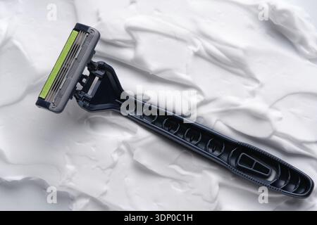 Black disposable razor on white shaving foam background Stock Photo