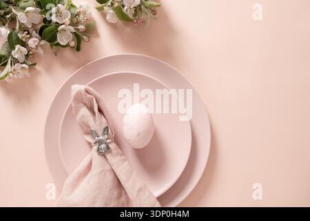 Minimal pastel Easter table composition with decorated egg and linen napkin with silver bunny ring on plate. Stock Photo