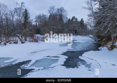 Winter river with partially frozen ice chunks flows through a snowy forest scene Stock Photo
