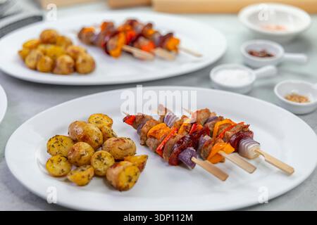 Pork kebabs with bell peppers, onions, and roasted potatoes served on a white plate Stock Photo