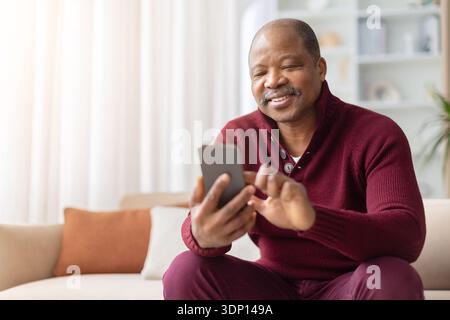Smiling mature black man using smartphone while sitting on sofa at home Stock Photo